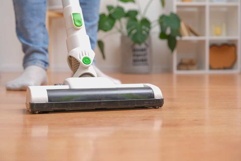 vacuuming wood look vinyl flooring in living room with bookshelf and plant